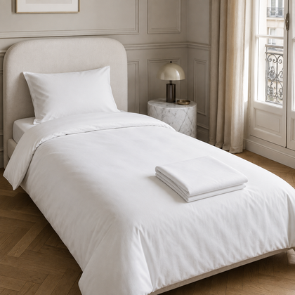Housse de couette blanche professionnelle presentee sur un lit une place dans une chambre elegante, avec du linge blanc plie sur le lit.