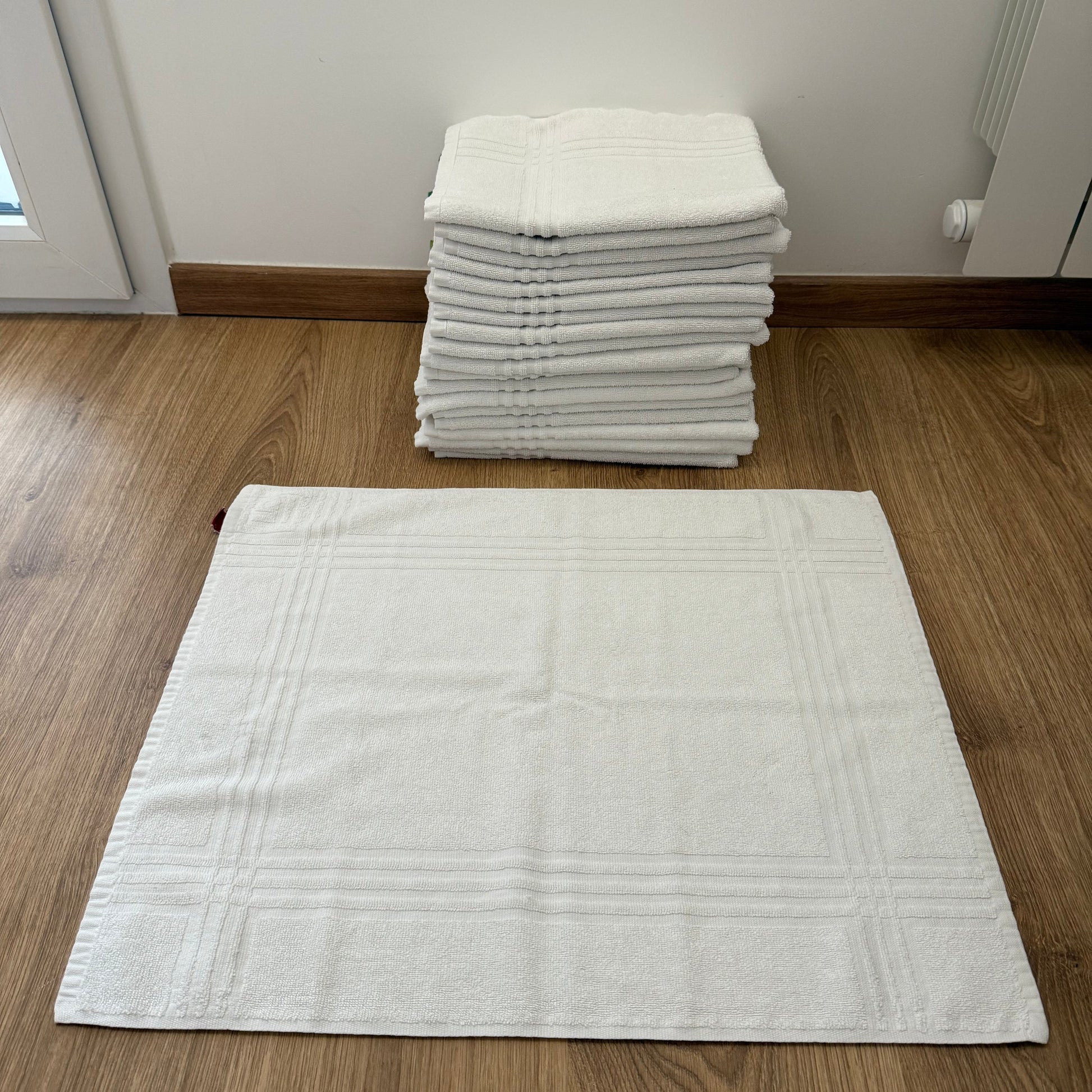 Tapis de bain blanc en coton, motif grec tissé, disposé au sol dans une salle de bain élégante. Parfait pour un usage hôtelier ou résidentiel haut de gamme.