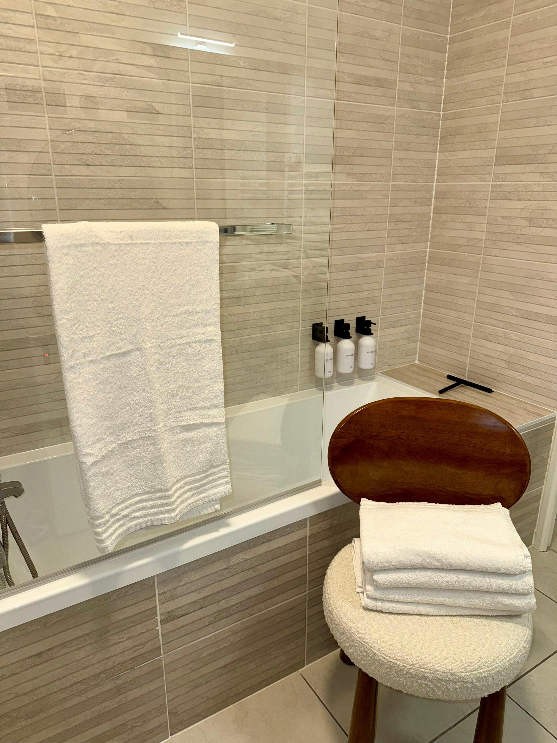 Salle de bain moderne avec serviette de bain recyclée de 70x140 cm, Eco Wayve, accrochée et pliée sur une chaise, parfait pour une ambiance élégante et écologique.